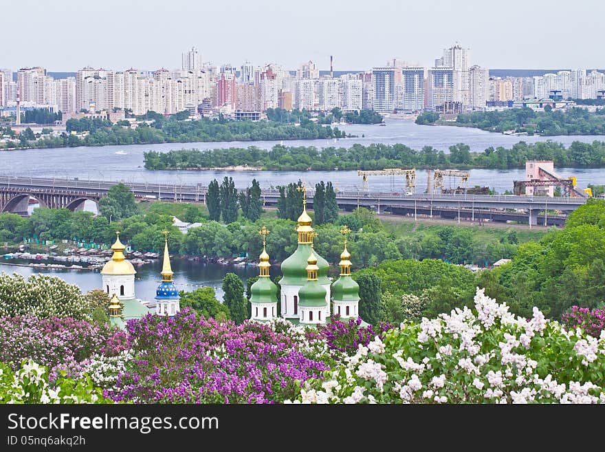 View on domes of Vydubychi monastery, blooming trees and high buildings on the left bank of Dniper in Kiev, Ukraine. View on domes of Vydubychi monastery, blooming trees and high buildings on the left bank of Dniper in Kiev, Ukraine