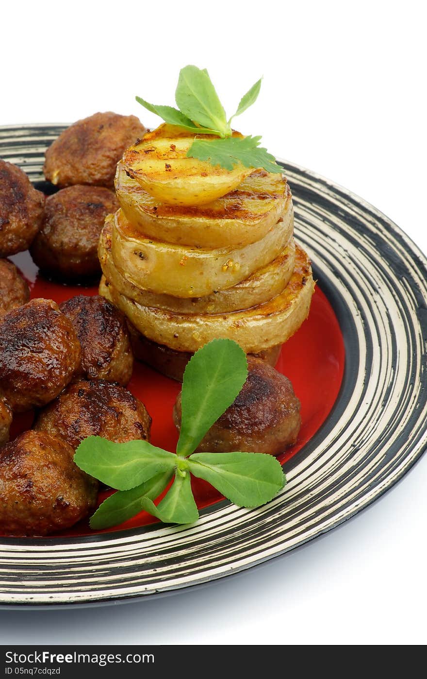 Roasted Meatballs and Stack of Grilled Potato with Greens on Red Striped Plate closeup on white background. Roasted Meatballs and Stack of Grilled Potato with Greens on Red Striped Plate closeup on white background