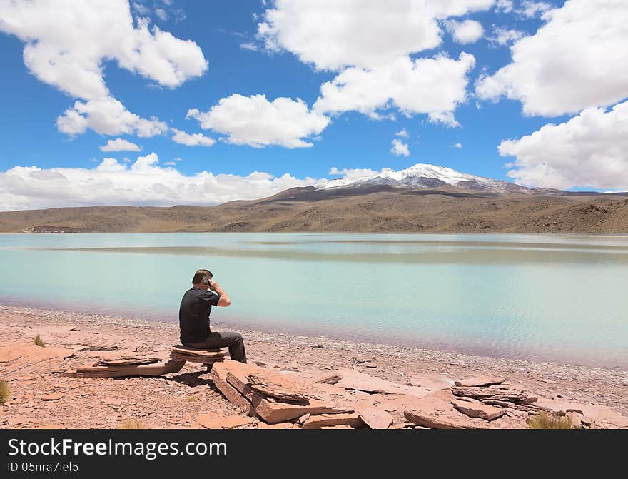 Man sitting on the shore of lagoon Celeste and talking on phone, Bolivia. Man sitting on the shore of lagoon Celeste and talking on phone, Bolivia