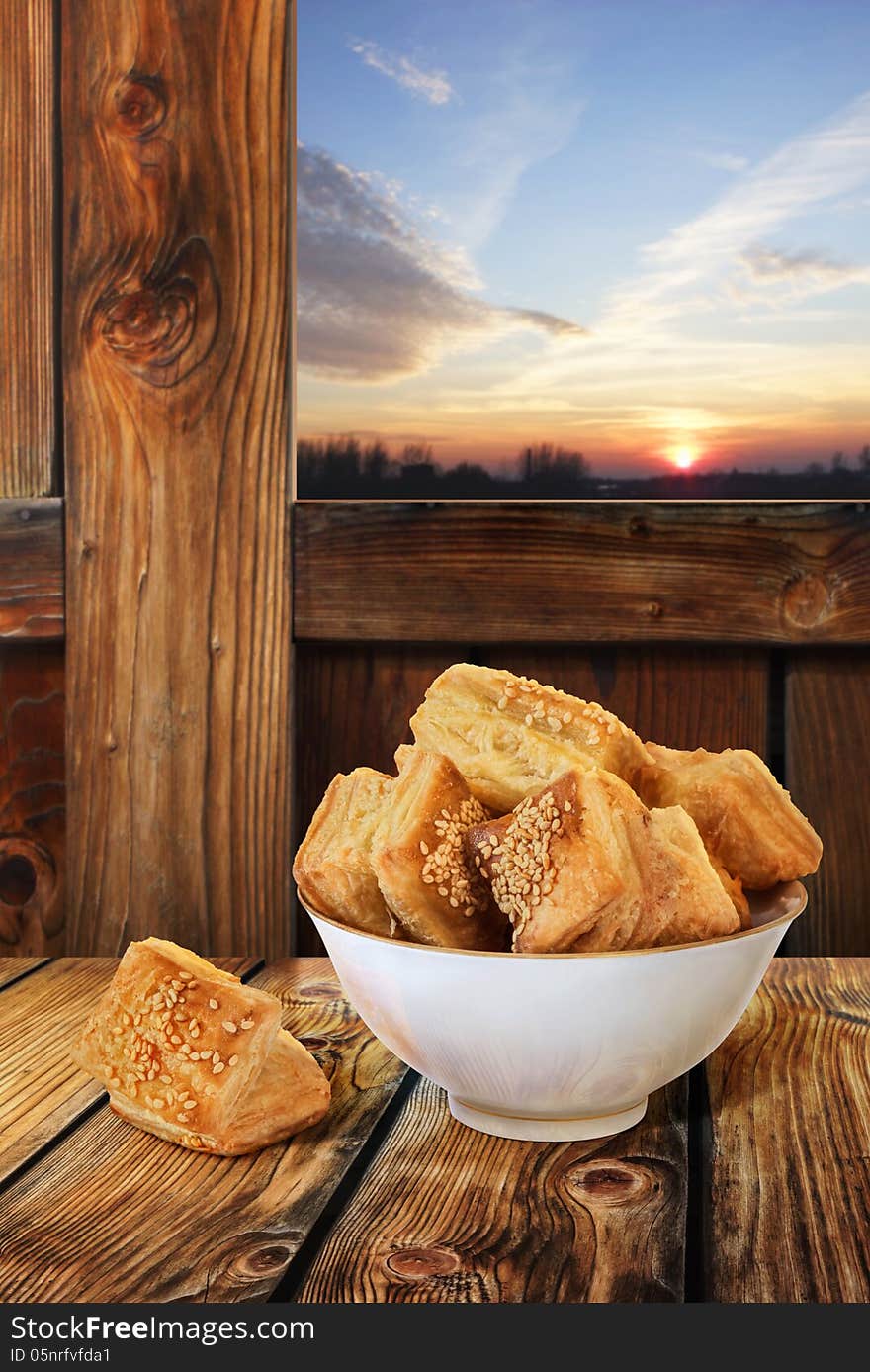 Small Square Sesame Puff Pastry Zu-Zu, served in white Porcelain Bowl, isolated with precise Clipping path, set in a wooden rustic farm ambient, with sunset sky in the background window. Small Square Sesame Puff Pastry Zu-Zu, served in white Porcelain Bowl, isolated with precise Clipping path, set in a wooden rustic farm ambient, with sunset sky in the background window.