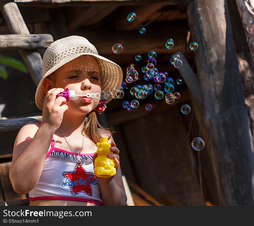 Little girl in a hat blowing soap bubbles