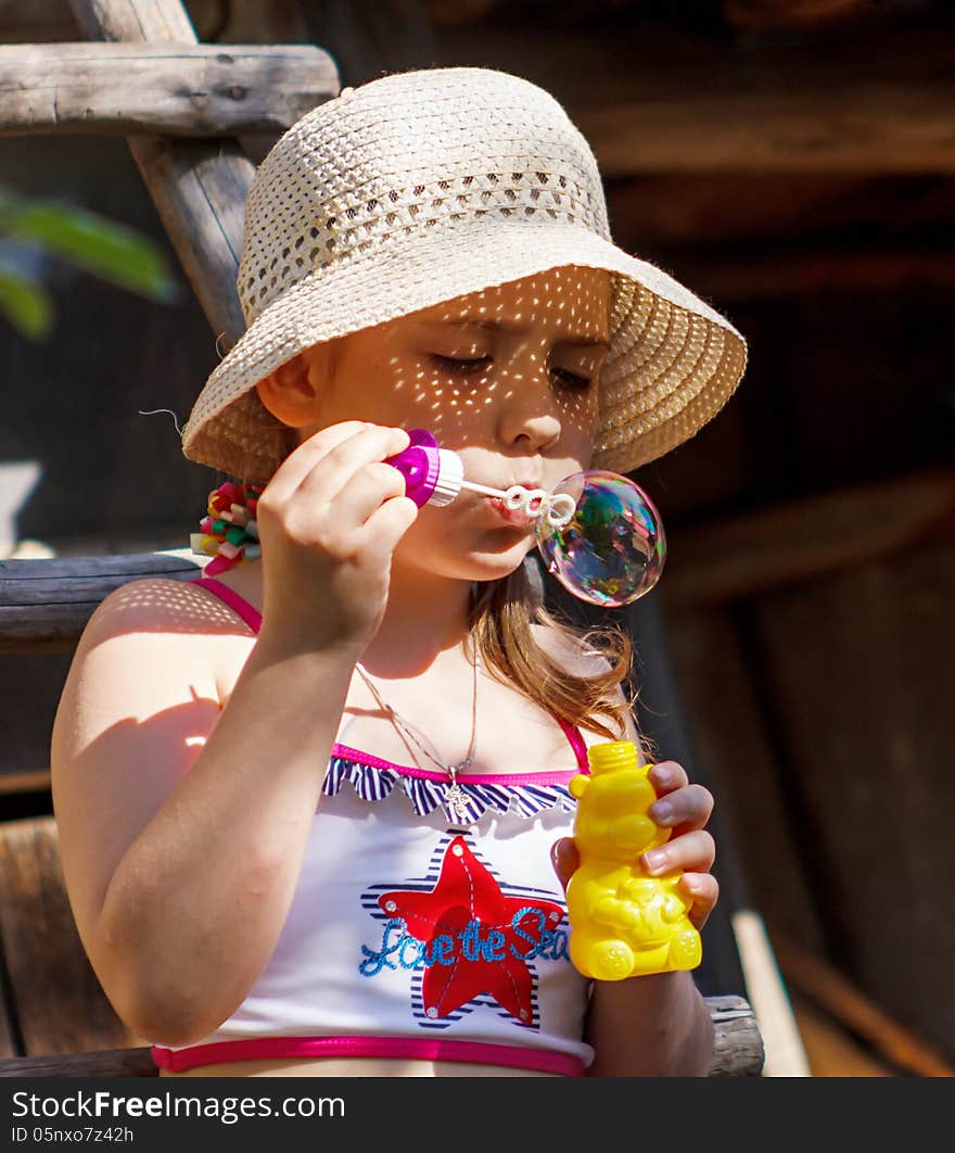 Little girl in a hat blowing soap bubble