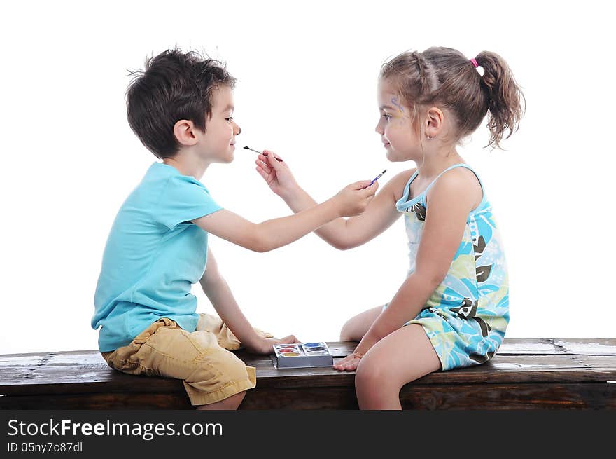 Boy and girl face painting one another siting on a bench in a studio on white background