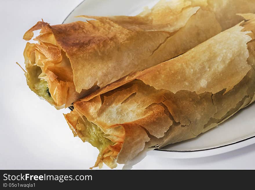 Roll pie with Spinach and cheese, on white oval plate with tiny blue rim. Roll pie with Spinach and cheese, on white oval plate with tiny blue rim.