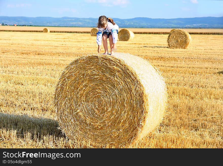 Small rural girl on the straw after harvest field with straw bales