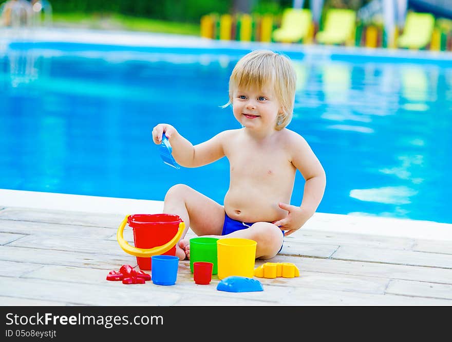 Positive kid playing with his toys by the swimming pool. Positive kid playing with his toys by the swimming pool