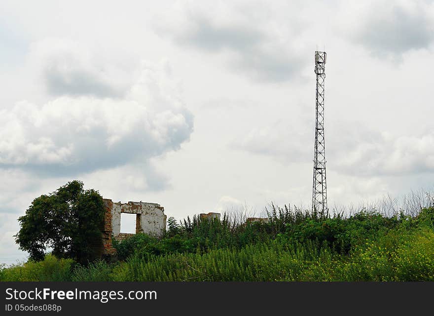 Telecommunication antenna tower among the ruins of brick buildings with cloudy sky