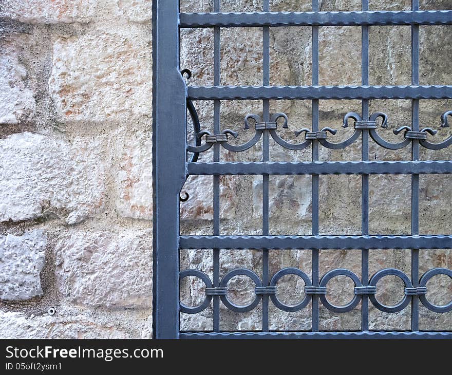 Fragment of wrought-iron door frame over ancient stone wall