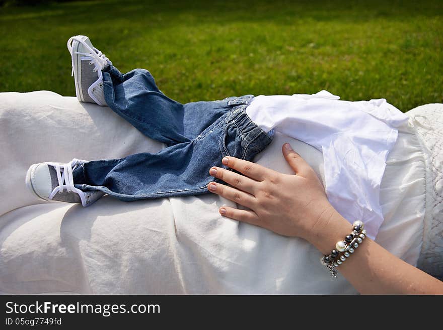 Belly Of A Pregnant Woman Holding Baby Clothes Close-up