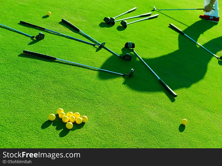 A lot of balls and golf clubs lying on green grass. A lot of balls and golf clubs lying on green grass