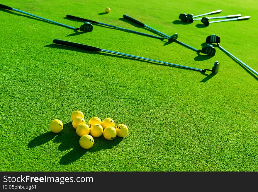 A lot of balls and golf clubs lying on green grass. A lot of balls and golf clubs lying on green grass