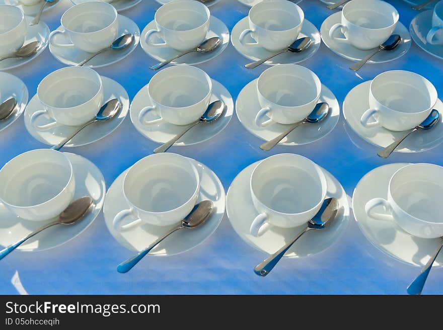 Stacked empty teacups with teaspoons at a function over white ba