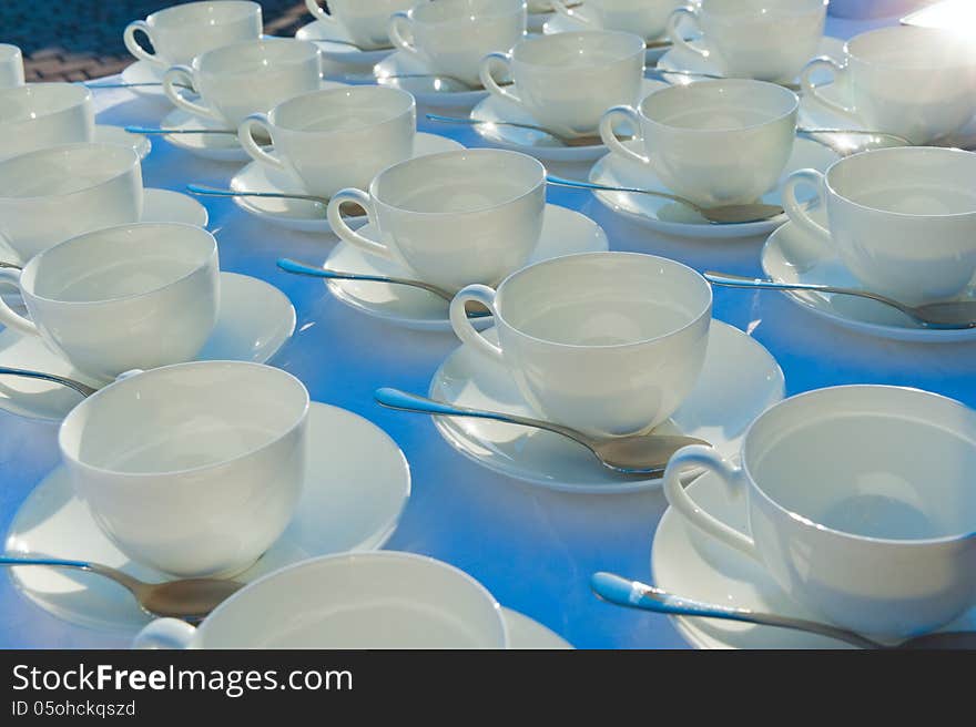 Stacked empty teacups with teaspoons at a function over white ba