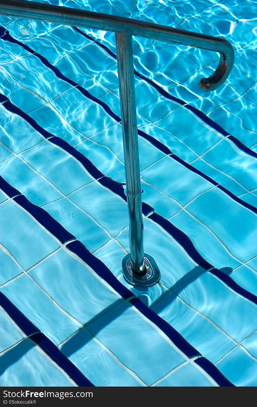 Light clear blue swimming pool with steel rail and tiled stairs.