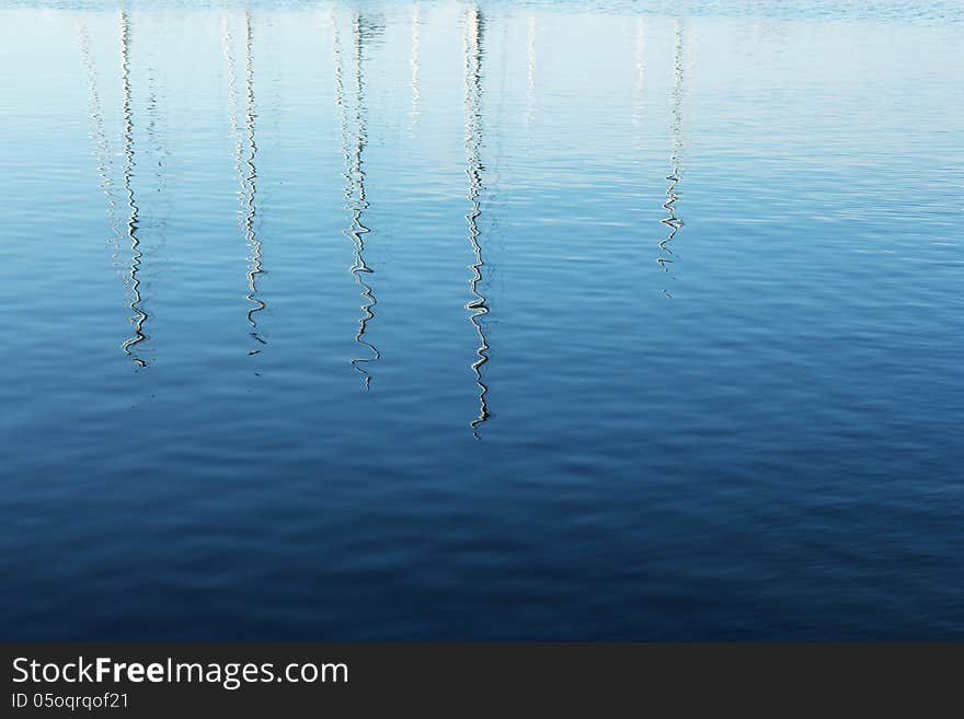 Masts of yachts reflected in blue water. Masts of yachts reflected in blue water