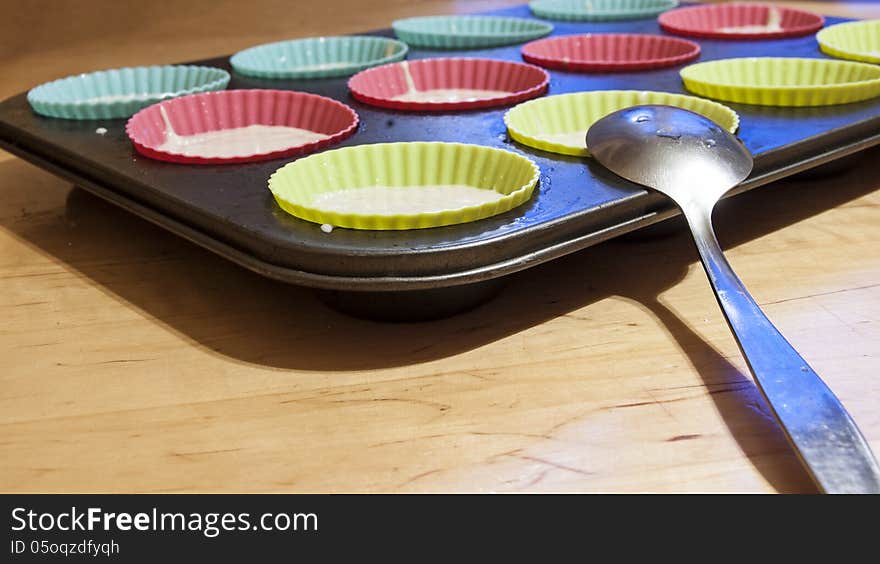 The process of making cupcakes. The dough is poured into a baking dish, near portioned spoon