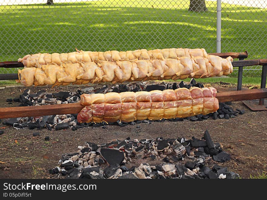 Fresh chicken and pork loin being roasted to a golden brown on a spit, over hot charcoal. Photo taken July 4, 2013. Fresh chicken and pork loin being roasted to a golden brown on a spit, over hot charcoal. Photo taken July 4, 2013.