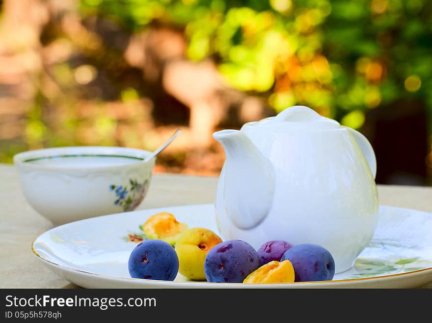 Summer morning tea - tea cup, teapot, plums and apricots on a platter