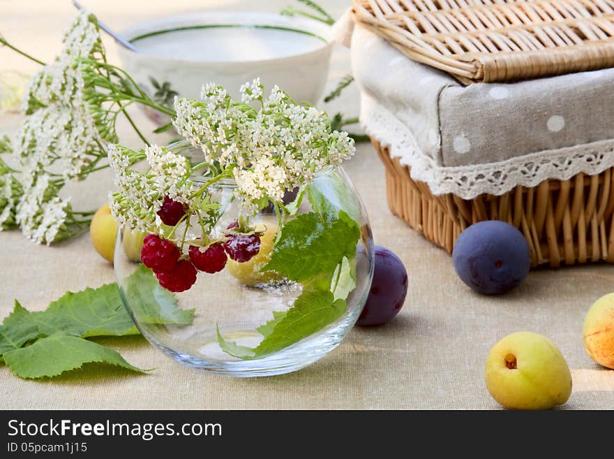 Bunch of raspberries in a glass bowl, plums, apricots, a cup of tea, basket of bread, and wildflowers. Bunch of raspberries in a glass bowl, plums, apricots, a cup of tea, basket of bread, and wildflowers