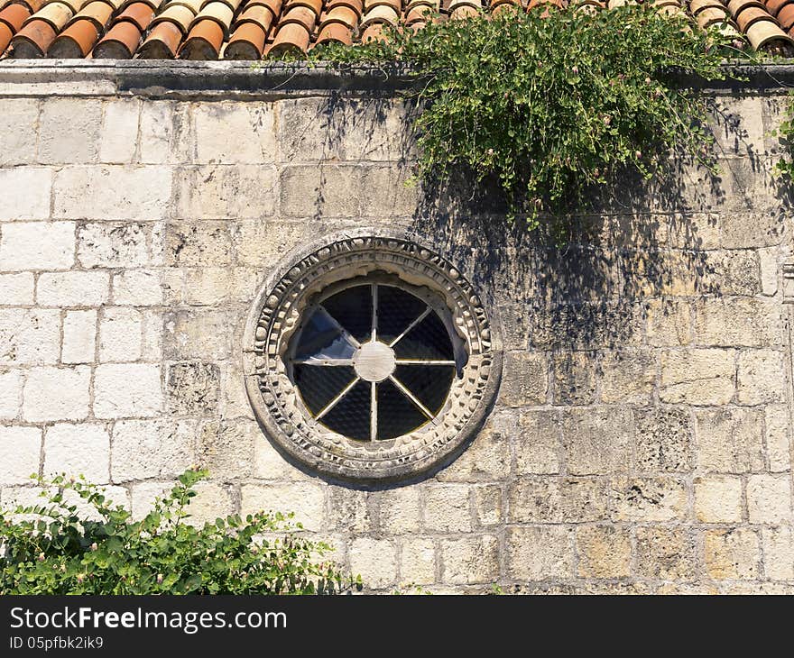 Fragment of ancient building stone wall with round shape window and green plants in Montenegro. Fragment of ancient building stone wall with round shape window and green plants in Montenegro