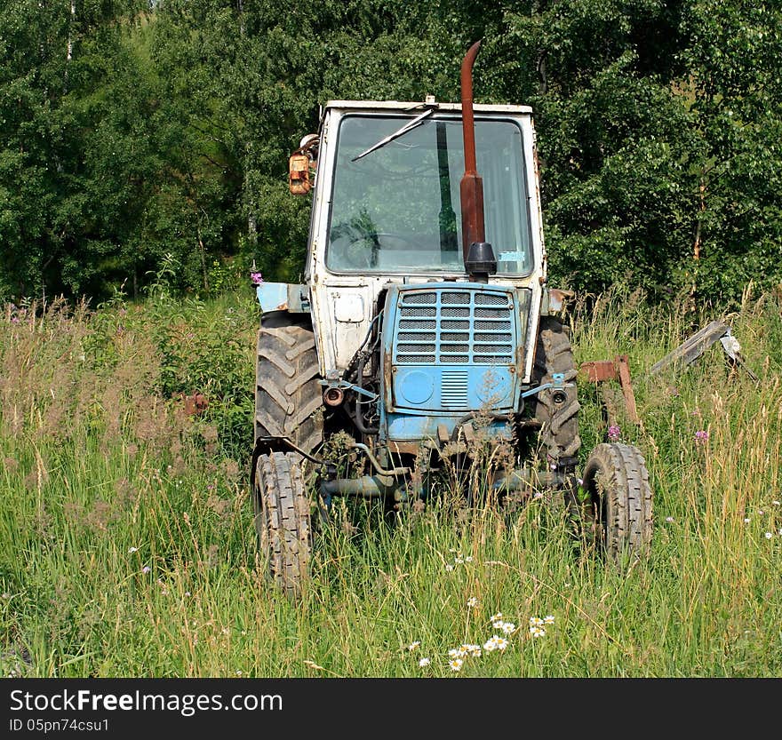 The old tractor in a field on a background of forest. The old tractor in a field on a background of forest