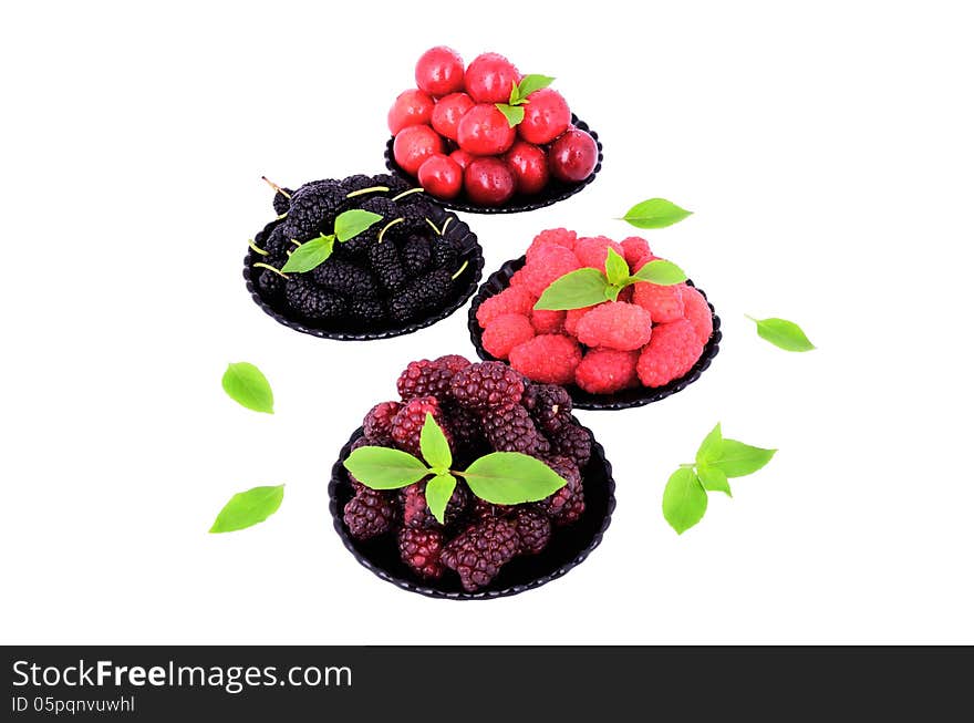 Mulberry; cherry; raspberry; blackberry in a plates close-up isolated on white; decorated with green leaves. Mulberry; cherry; raspberry; blackberry in a plates close-up isolated on white; decorated with green leaves.