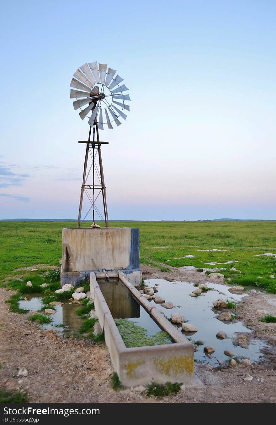 Landscape of windmill waterpump on green meadow at sunrise