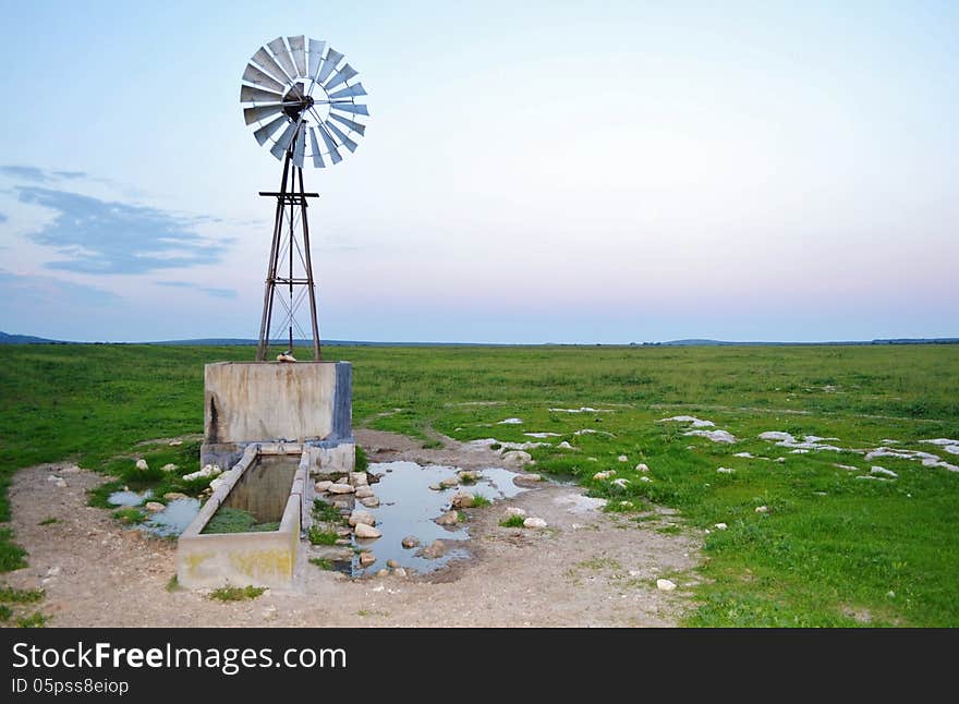 Landscape of windmill waterpump on green meadow at sunrise