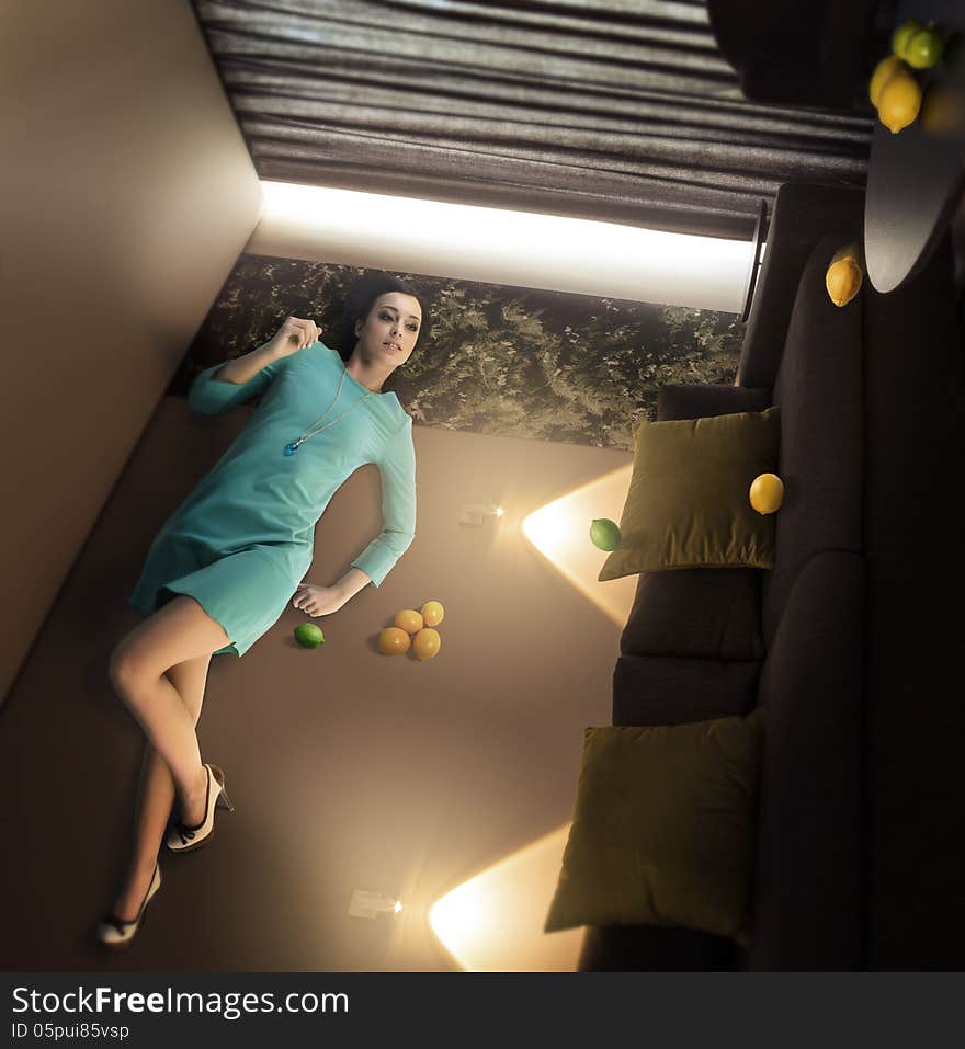 Extraordinary beautiful woman lying and relaxing on the wall in the overturned room with lemons