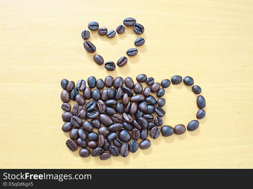 Coffee cup with heart image made up of coffee beans on wood background