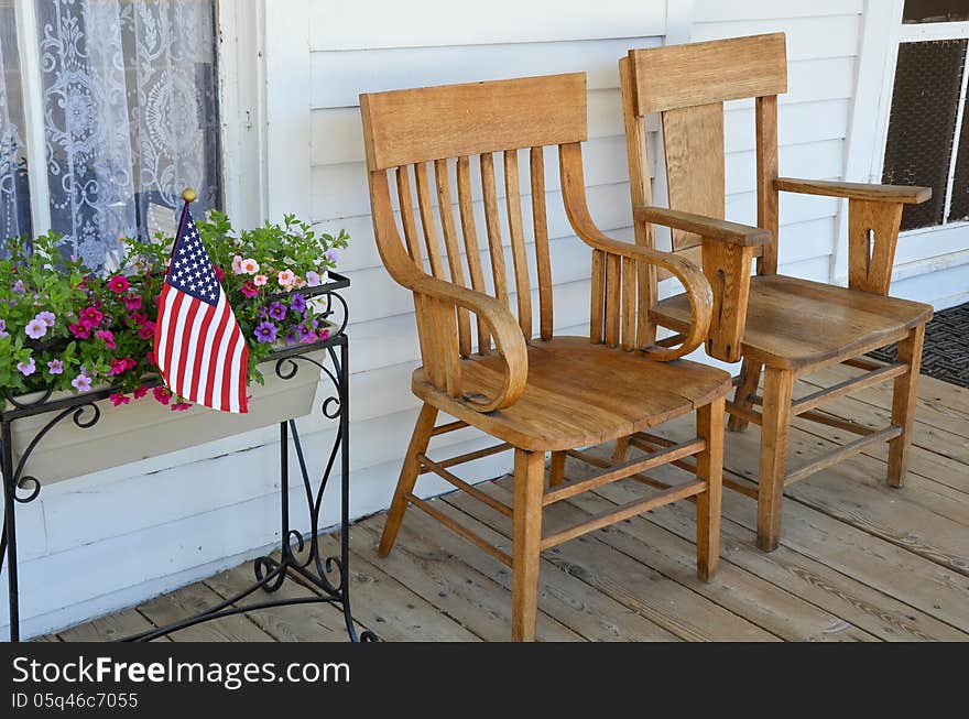 Two wooden chairs on old front porch with flowers and american flag. Two wooden chairs on old front porch with flowers and american flag