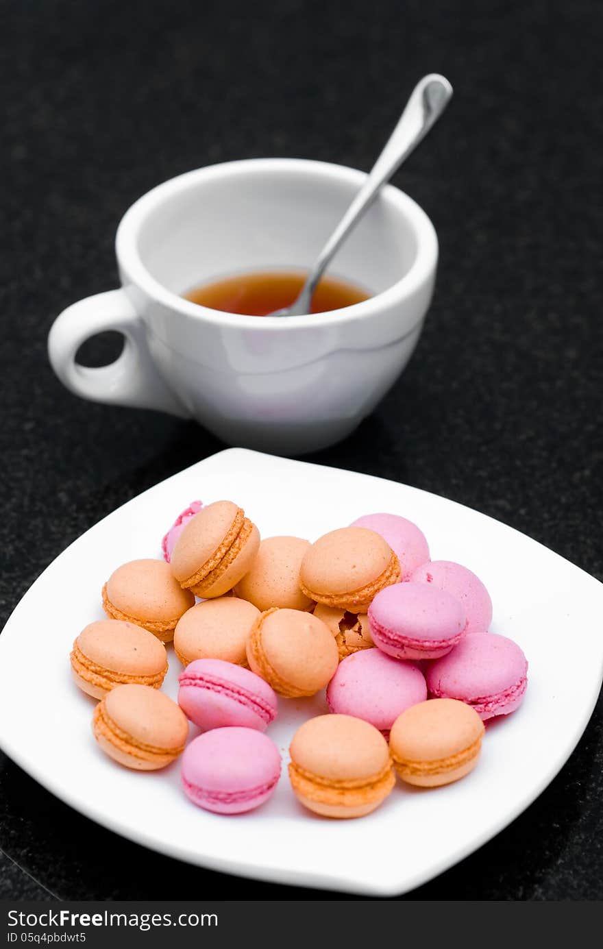 Pile of pink and orange macaroon in a plate with a cup of tea on black table. Pile of pink and orange macaroon in a plate with a cup of tea on black table