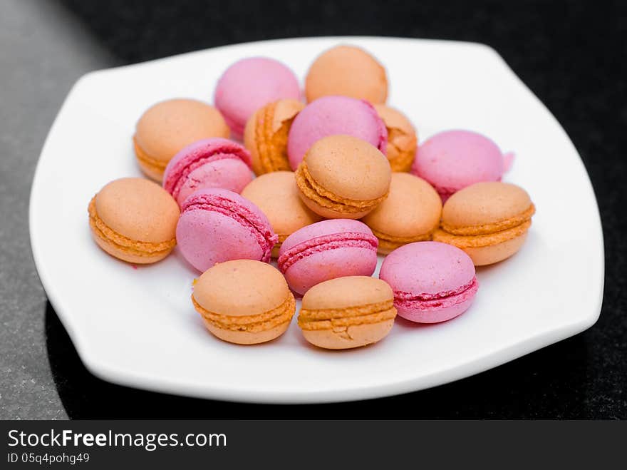 Heap of macaroons in white plate on black background