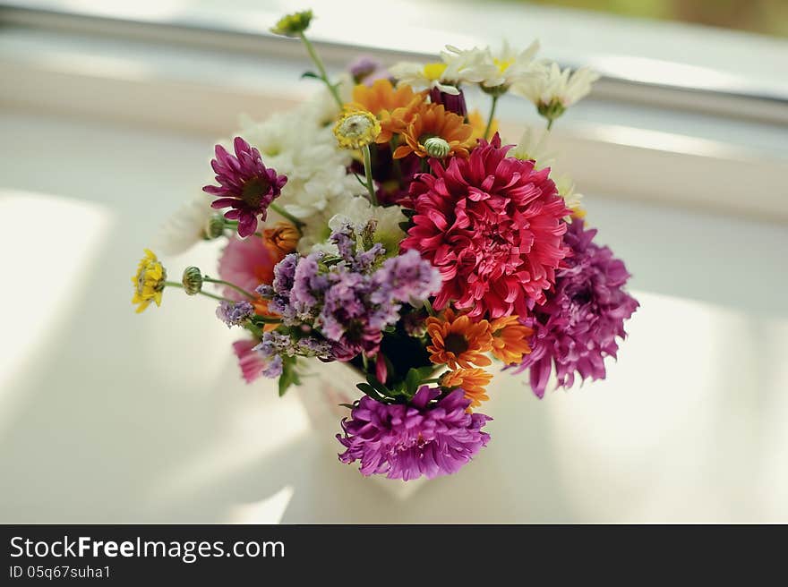 On the window sill is a bouquet of pink roses in a beautiful decorative vase. On the window sill is a bouquet of pink roses in a beautiful decorative vase