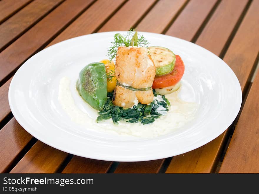 Grill fish in roll serve with tomato and yellow and green bell pepper on white plate