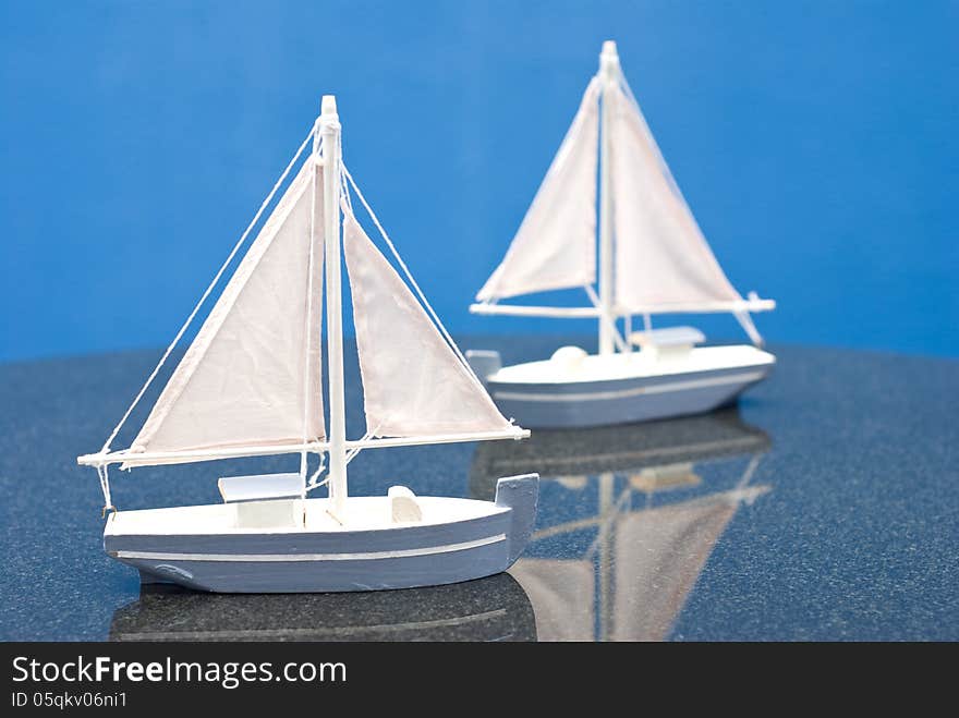 Two small blue and white wooden sailboat models on table with blue background. Two small blue and white wooden sailboat models on table with blue background