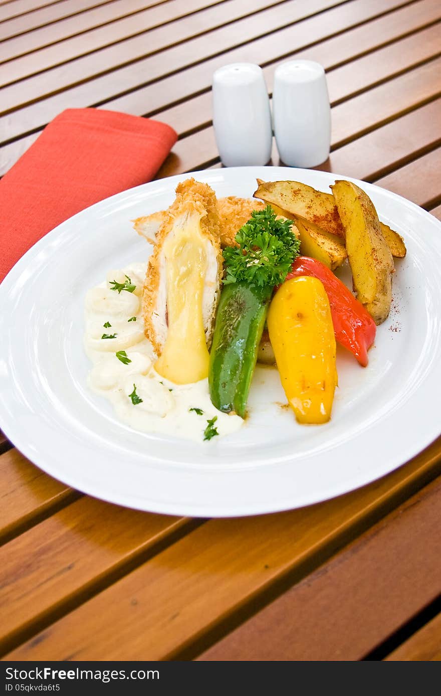 Stuff chicken serve with green yello and red bell pepper and fried potato in white plate on wood table