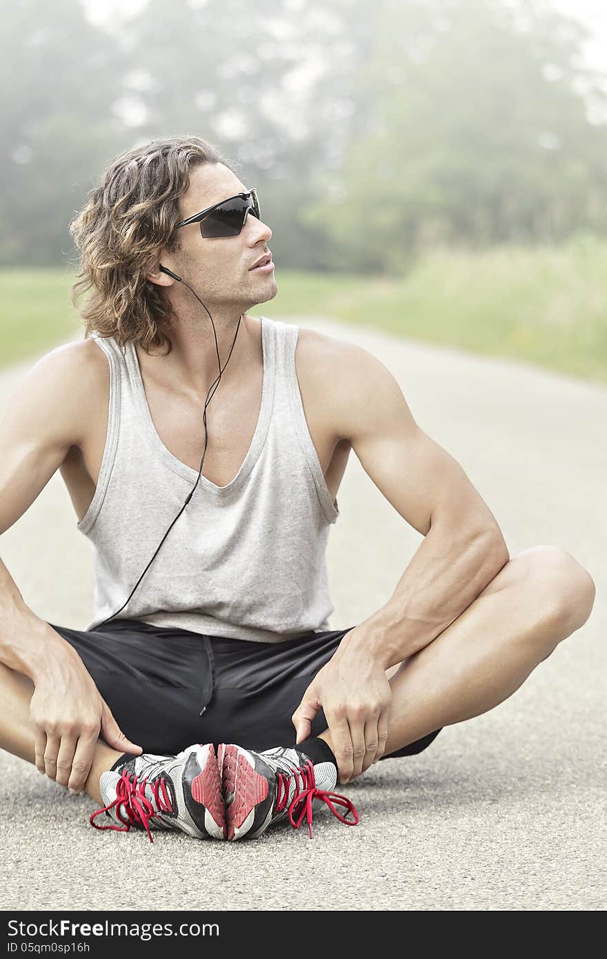 Athlete stretches his leg sitting down and smiling. Athlete stretches his leg sitting down and smiling