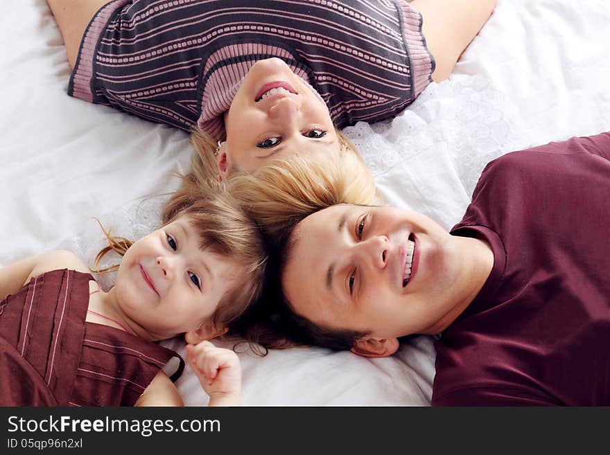 Happy Father, Little Daughter And Mother Lie On Bed