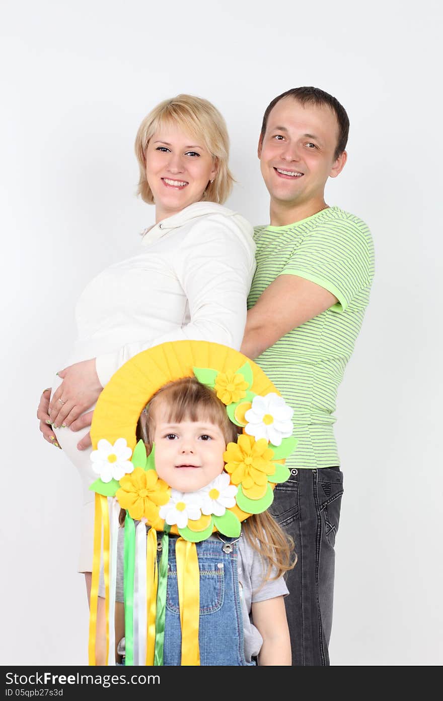 Happy pregnant wife and husband hold belly and little daughter stands near them on white background. Focus on parents. Happy pregnant wife and husband hold belly and little daughter stands near them on white background. Focus on parents.