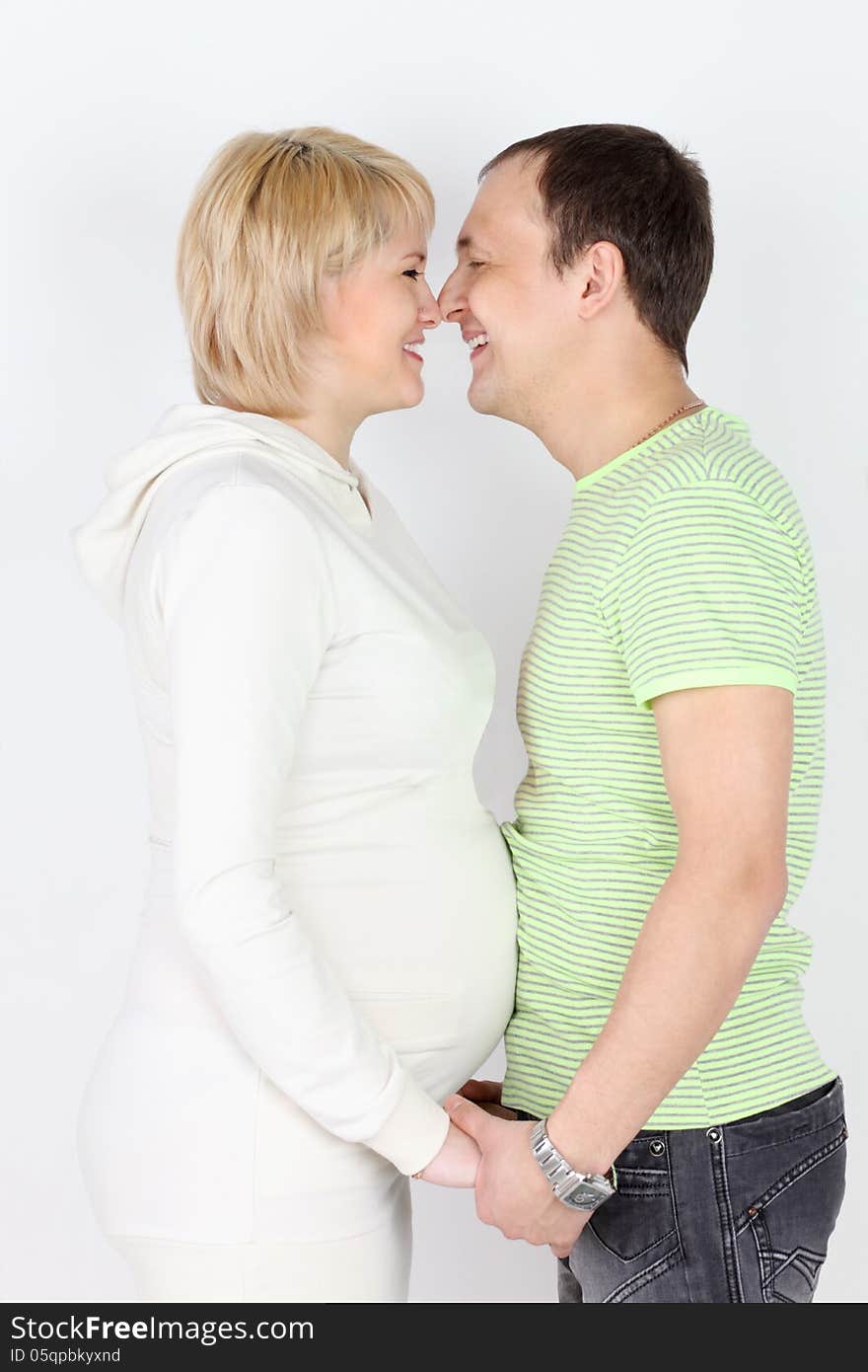 Happy pregnant wife and husband touch each other noses and laugh on white background.