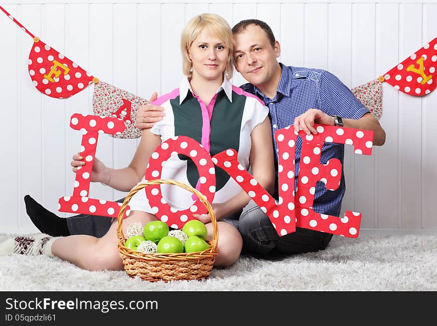 Happy pregnant wife and husband sit on carpet and hold letters L O V E.