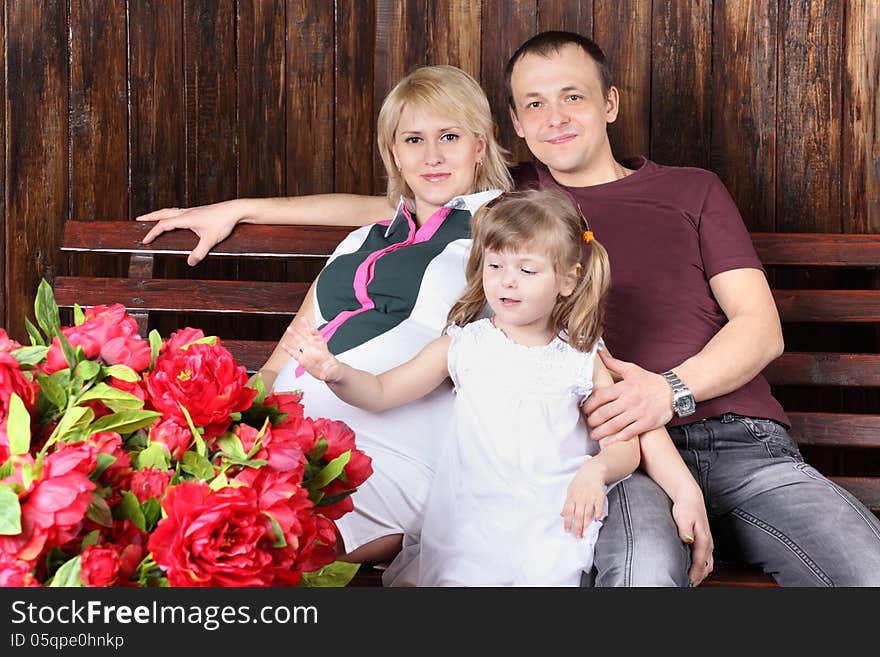 Father, pregnant mother and little daughter sit on bench next to large bouquet of flowers. Father, pregnant mother and little daughter sit on bench next to large bouquet of flowers.