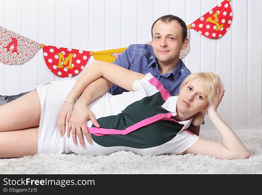 Happy pregnant wife and husband lie on carpet