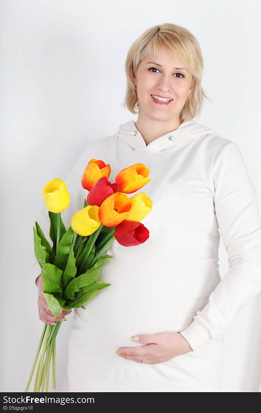 Happy pregnant woman in white with bouquet of tulips on white background.