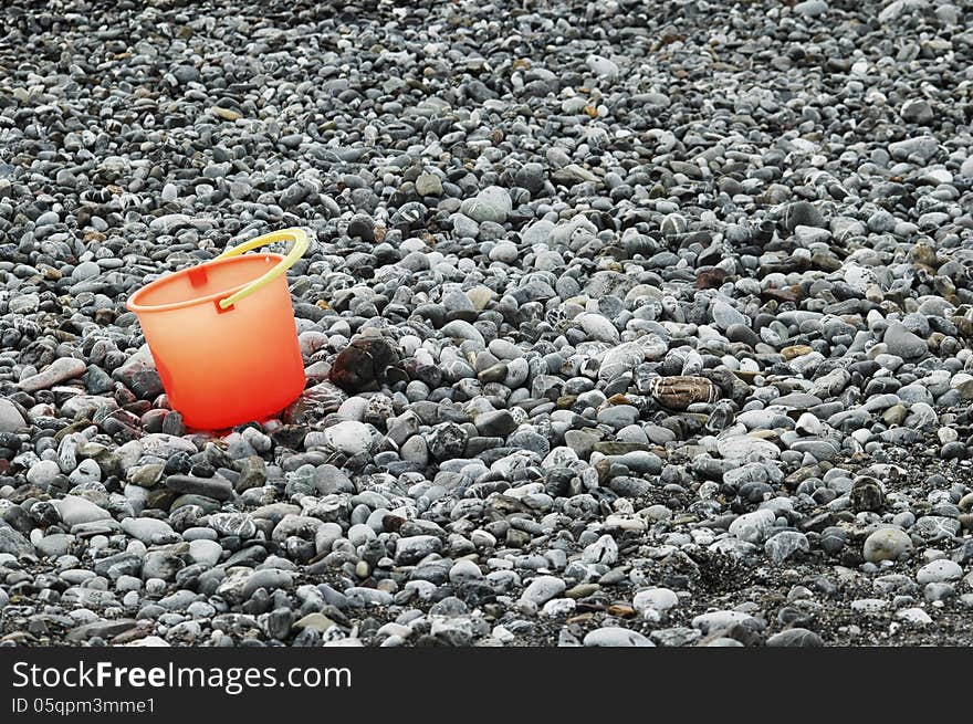 One orange bucket on the beach alone