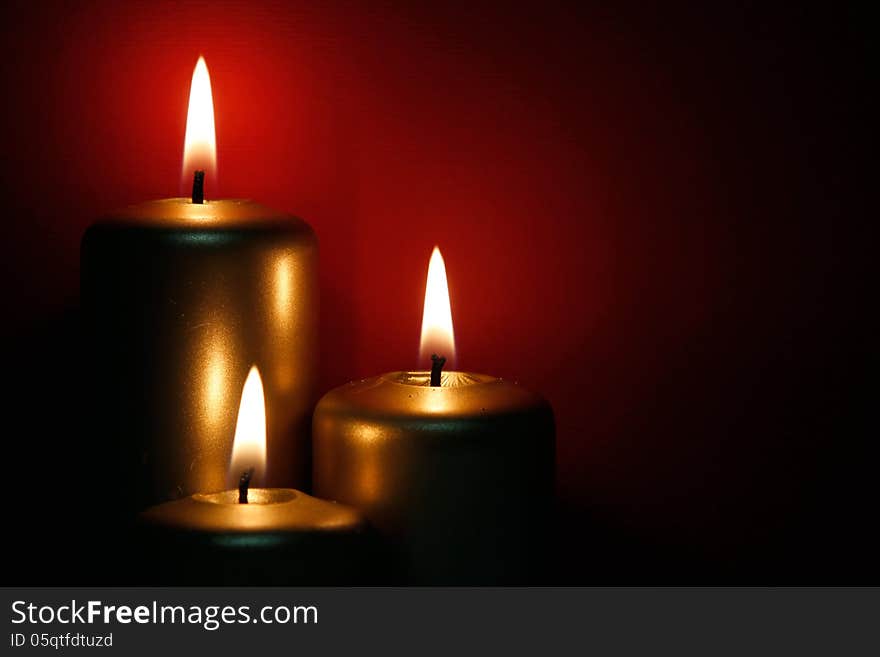 Three burning gold candles on the red background. Three burning gold candles on the red background