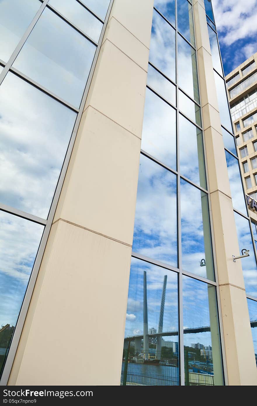 In windows of the modern building are reflected the blue sky and clouds