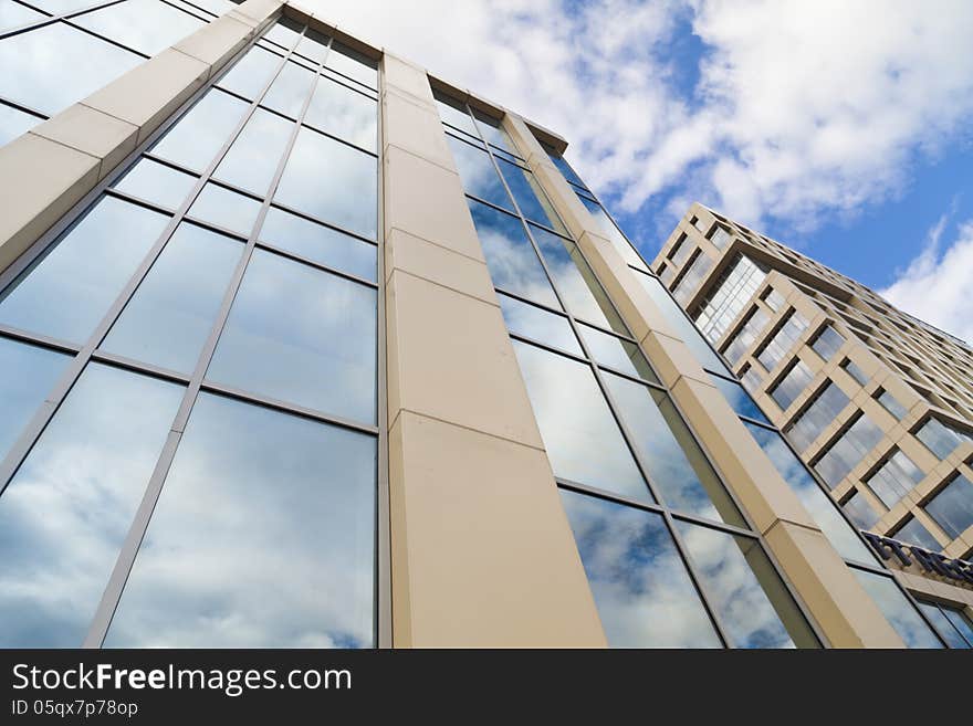 In windows of the modern building are reflected the blue sky and clouds