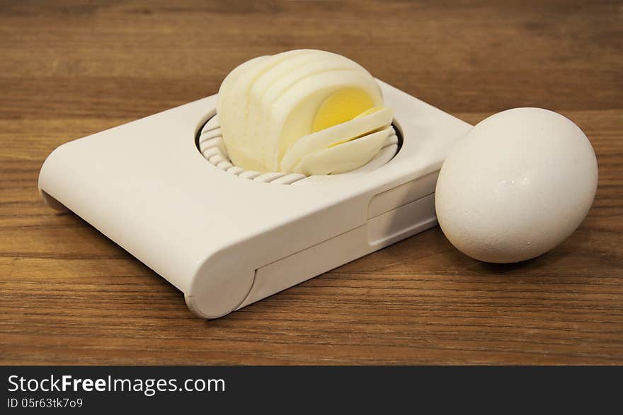 Egg next to boiled egg in egg slicer against a brown wood grained background. Egg next to boiled egg in egg slicer against a brown wood grained background